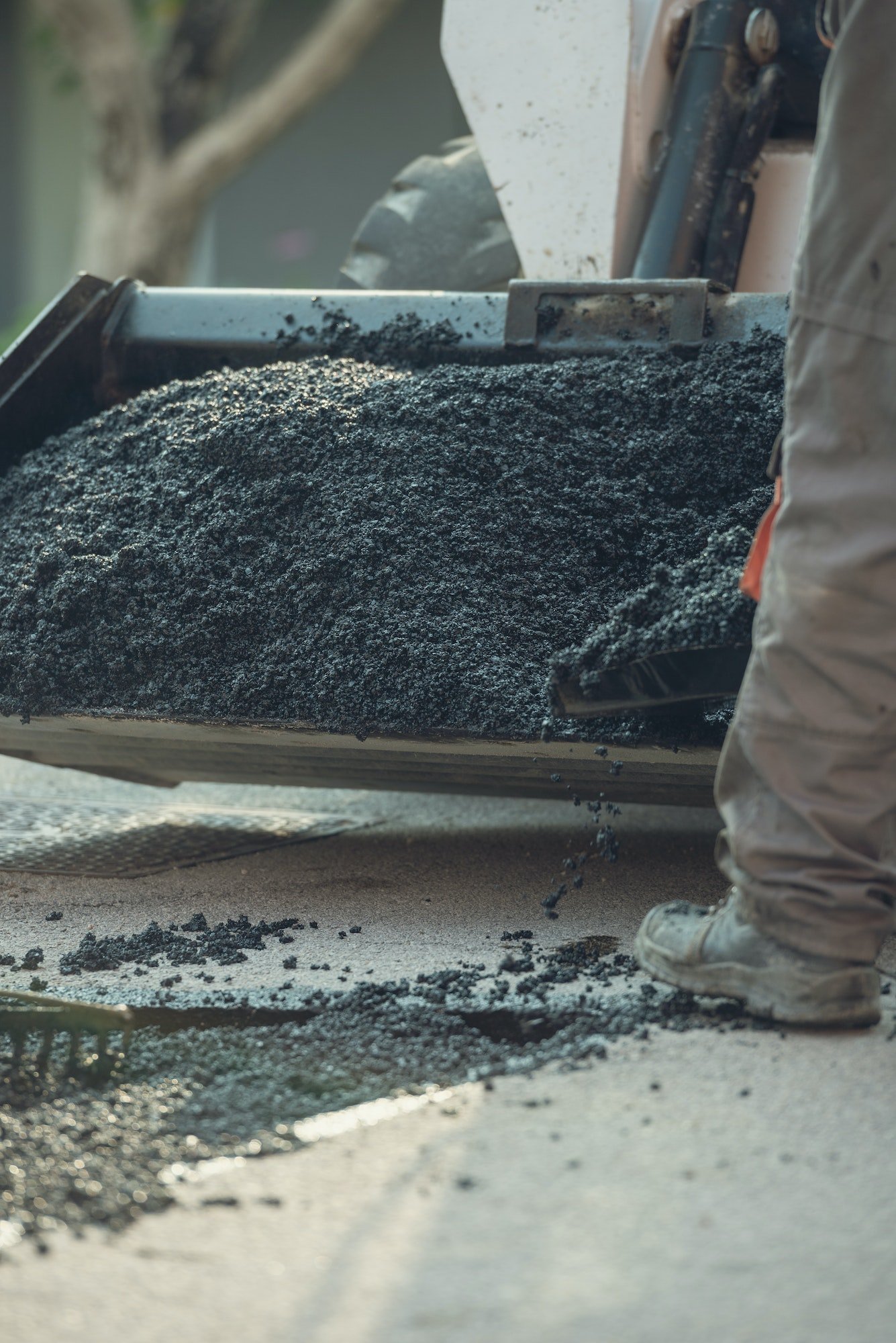 Retro image of a worker taking asphalt mix with a shovel from a wheelbarrow